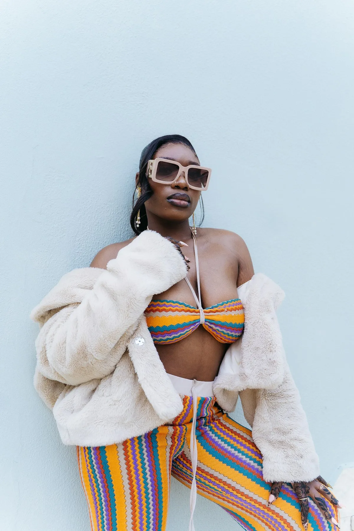Stylish woman posing confidently in a bold colorful outfit with oversized sunglasses and a faux-fur coat