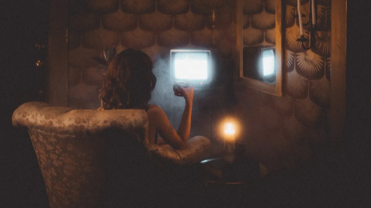 Person relaxing on a couch watching television at home, warm evening light
